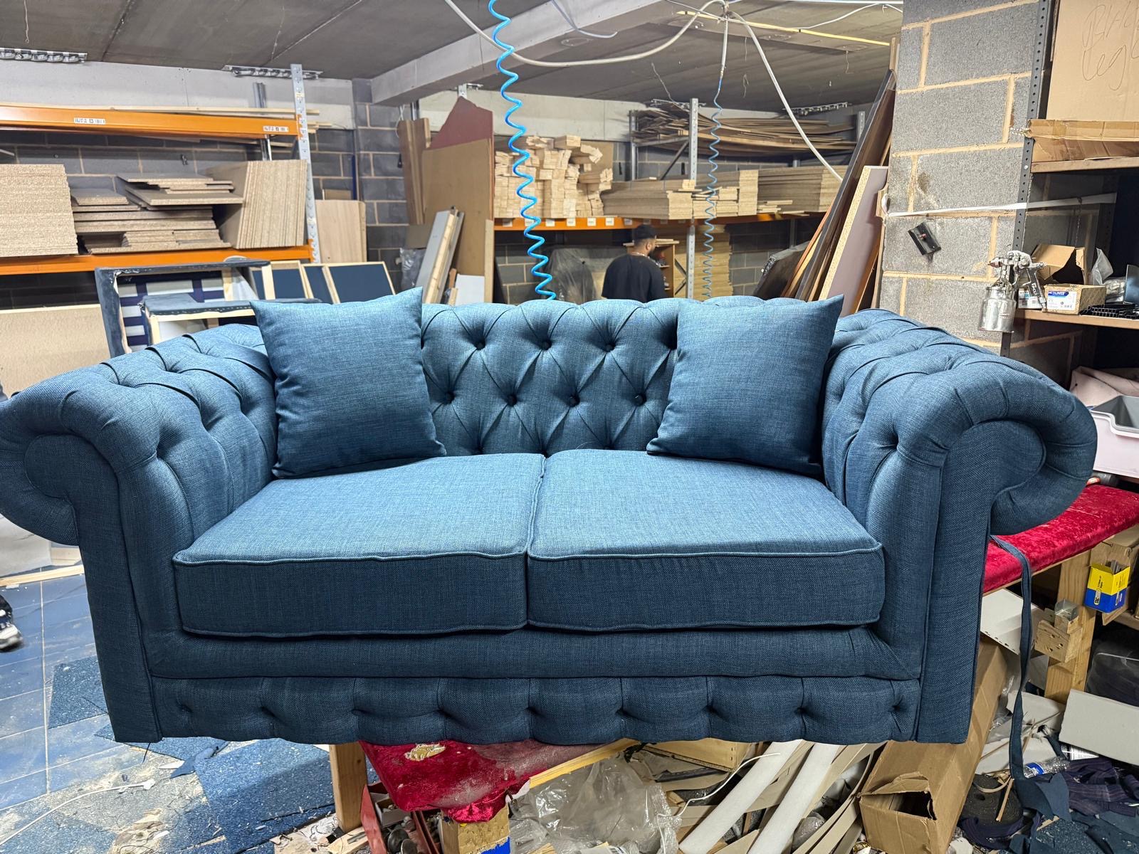 Blue button-tufted sofa with rolled arms in a workshop.