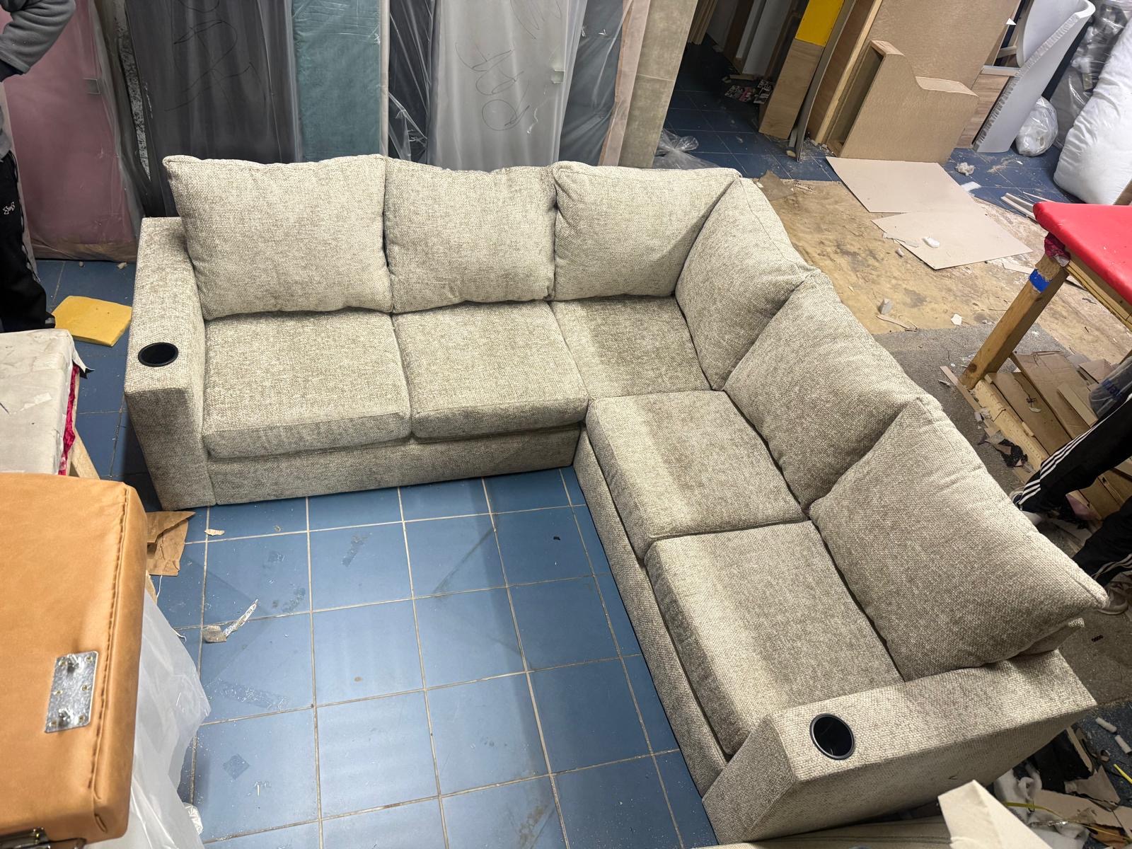 Neutral corner sofa with cup holders in its arms, photographed in a workshop.