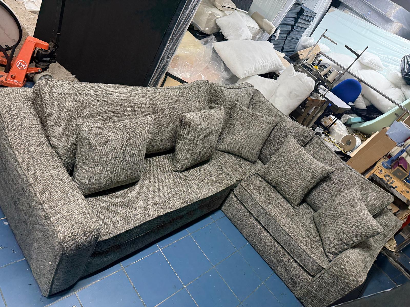 Grey corner sofa with loose cushions in a workshop.