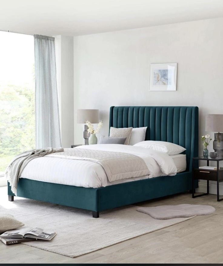 Teal upholstered bed with a vertically padded headboard in a bright room.