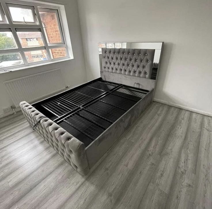 Grey upholstered bed frame with a button-tufted headboard and an exposed metal mattress support.