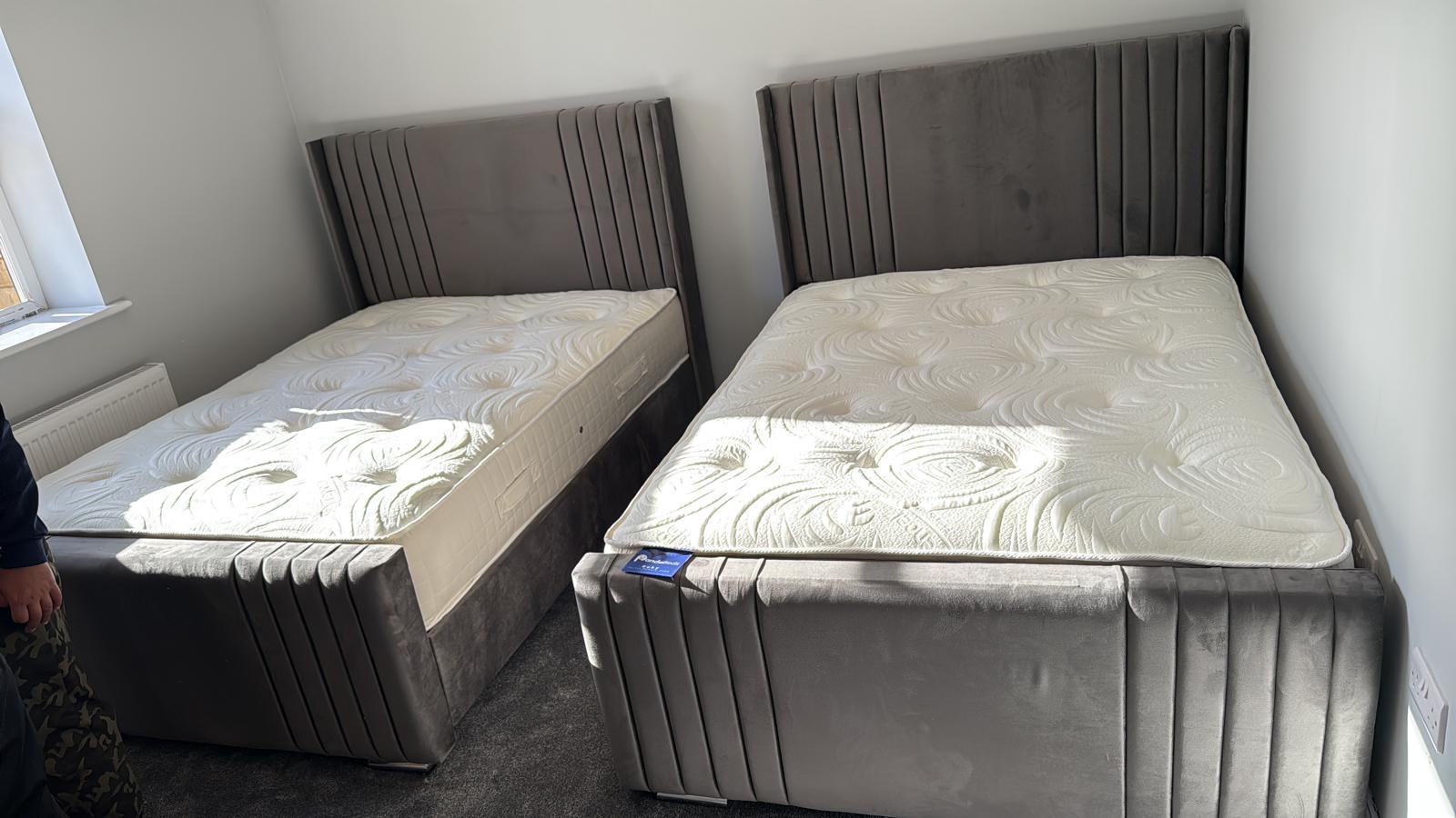 Two grey upholstered bed designs with vertical padded detailing.